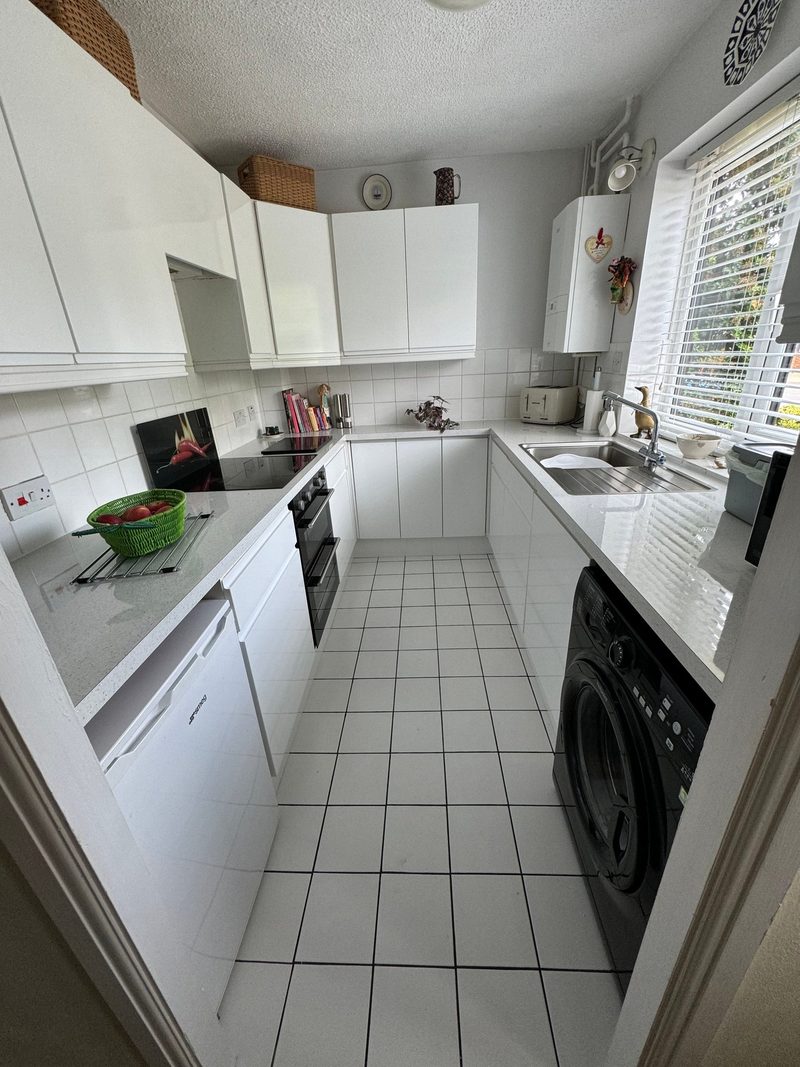 Galley kitchen in Emerson Valley after the work: white gloss handle-free doors, a light speckled worktop and a new sink under the window