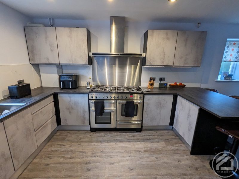 Kitchen in Monkston Park after the work: concrete-effect doors, a dark worktop, a range cooker and a stainless steel splashback