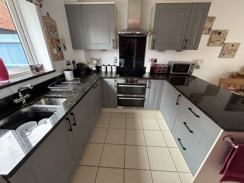 Kitchen in Oakridge Park after new doors, panels and handles: grey framed doors with black bar handles and a black speckled worktop