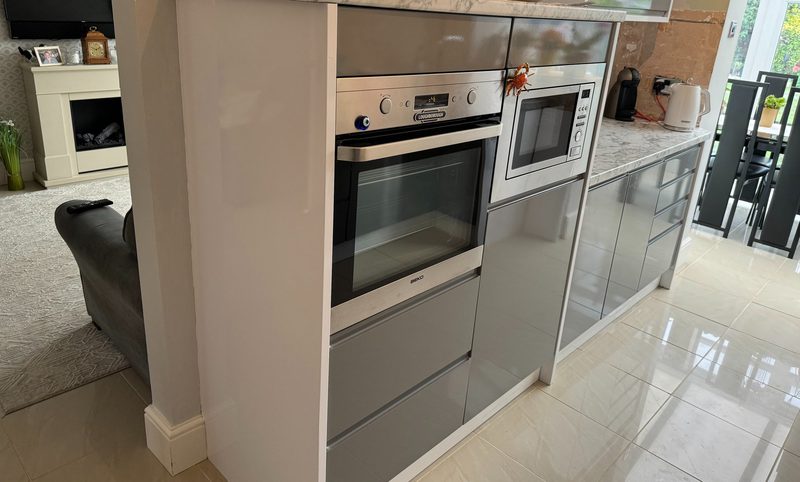 Kitchen in Towcester after new doors and plinths: grey gloss handle-free doors, a built-in oven and microwave and a white marble-effect worktop