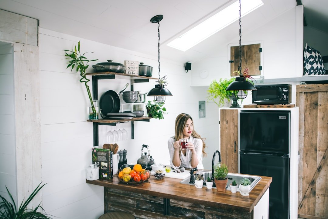 Woman sitting at a wooden kitchen counter with open shelves of pans behind her